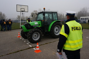 Policjant obserwuje jazdę sprawnościową ciągnikiem  rolniczym z zamontowanym na masce „talerzem Stewarta”.