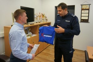 I Zastępca Komendanta Powiatowego Policji w Zawierciu wręcza młodemu mężczyźnie niebieską torbę z logo kampanii „nie reagujesz – akceptujesz” z zawartości drobnych upominków.