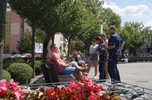 Policjantka, Policjant i przedstawicielka Centrum Rozwoju Lokalnego rozmawiają i przekazują materiały infromacyjne - ulotki siedzącym na ławce osobom.