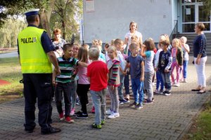 Policjant rozmawia z grupą dzieci przed przejściem dla pieszych.