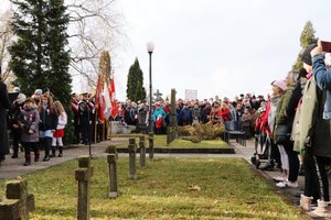 Uczestnicy uroczystości zgromadzeni na cmentarzu. Na pierwszym planie rząd krzyży.