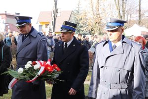 Delegacja w składzie Komendant Powiatowy Policji w Zawierciu - insp. Jacek Kurdybelski, Zastępcy Komendanta Powiatowego Państwowej Straży Pożarnej w Zawierciu mł. bryg. Łukasza Osikowicza i I Zastępcy Komendanta Powiatowy Policji w Zawierciu mł.insp. Arkadiusza Miśty.
Idący w środku Zastępca Komendanta Powiatowego Państwowej Straży Pożarnej w Zawierciu mł. bryg. Łukasz Osikowicz niesie w ręku wiązankę kwiatów.
