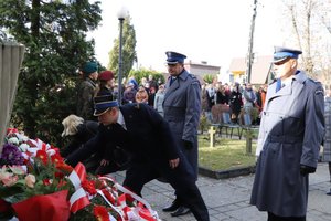 Zastępca Komendanta Powiatowego Państwowej Straży Pożarnej w Zawierciu mł. bryg. Łukasz Osikowicz składa przed Pomnikiem Niepodległości wiązankę kwiatów. Obok niego stoi Komendant Powiatowy Policji w Zawierciu - insp. Jacek Kurdybelski i I Zastępca Komendanta Powiatowego Policji w Zawierciu mł.insp. Arkadiusz Miśta.