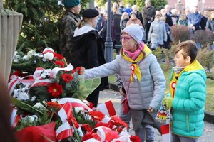 Dziewczynka w towarzystwie małego chłopczyka składa kwiaty przed Pomnikiem Niepodległości.