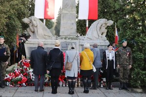 Grupa osób oddająca hołd po złożeniu kwiatów przed Pomnikiem Niepodległości.