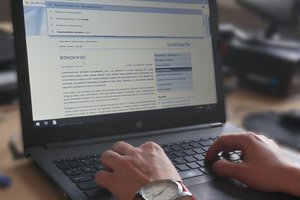 Widoczne dłonie osoby piszącej na klawiaturze laptopa.
