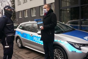 Prezydent Zawiercia Łukasz Konarski przekazuje kluczyki do radiowozu umundurowanemu policjantowi. W tle widoczny oznakowany radiowóz.