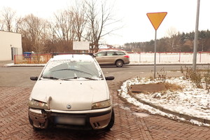 Na zdjęciu widoczny samochód osobowy z roztrzaskanym z prawej strony błotnikiem i lampą. Po prawej stronie widoczny pionowy znak drogowy - ustąp pierwszeństwa przejazdu. W tle widoczny przejeżdżający samochód.