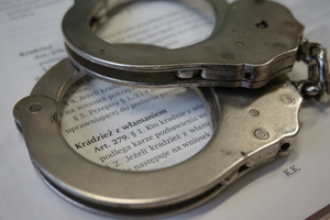 Na zdjęciu widoczne kajdanki położone na otawrtym kodeksie karnym. W tle widać zapis artykułu 279 kodeksu karnego - kradzież z włamaniem.