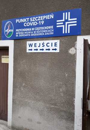 Na zdjęciu widoczna tablica informacyjna przy wejściu do budynku: Punkt szczepień COVID-19. Przychodnia w Częstochowie. Samodzielny Publiczny Zakład Opieki Zdrowotnej Ministerstwa Spraw Wewnętrznych i Administracji w Katowicach imienia sierżanta Grzegorza Załogi. Poniżej napis Wejście.