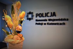 Na pierwszym planie świąteczny stroik, w tle napis Komenda Wojewódzka Policji w Katowicach i policyjne logo.