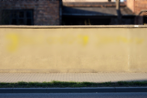 Na zdjęciu widoczny mur, na którym żółtą farbą namalowano napis (napis został rozmyty).