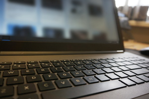 Na zdjęciu widoczna klawiatura laptopa. W tle rozmyty obraz ekranu.