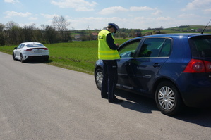 Na zdjęciu widać umundurowanego policjanta w kamizelce odblaskowej z napisem POLICJA stojącego przy samochodzie osobowym. W tle widoczny nieoznakowany radiowóz.