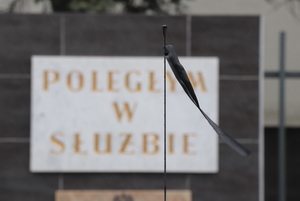 Tablica pamiątkowa z napisem: Poległym w służbie, na tle której widoczna jest czarna wstążka przypięta do anteny radiowozu.