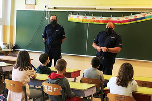 Na zdjęciu widoczny dwóch umundurowanych policjantów, którzy prowadzą prelekcję dla siedzących przed nimi dzieci.
