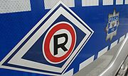 Na zdjęciu widoczne oznakowanie odblaskowe radiowozu - symbol Ruchu drogowego (Symbol graficzny w kształcie rombu. W środku znajduje się białe koło, w którym widnieje duża litera R. Białe koło otoczone jest czerwoną obwódką. Całość znajduje się na tle granatowego rombu, który ma białą szeroką obwódkę, a następnie cienką granatową.) i policyjna gwiazda w tle.