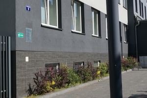 Na zdjęciu widoczny budynek Komendy Powiatowej Policji w Zawierciu, na którym zamieszczone zostało oznakowanie zielona, odblaskowa tabliczka z grafiką przedstawiającą serce z błyskaiwcą i plusem po prawej stronie oraz napisem AED i strzałką wskazującą kierunek