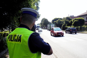 Na zdjęciu widoczny umundurowany policjant dokonujący pomiaru prędkości jadących pojazdów.