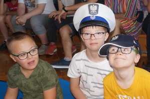 Na zdjęciu widoczni trzej chłopcy. Chłopiec po prawej stronie ma na głowie granatową policyjną czapkę. Chłopiec w środku ma na głowie czapkę policjanta ruchu drogowego.