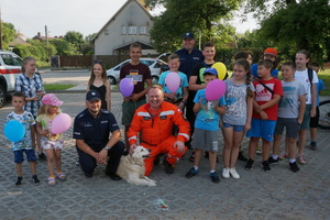 Zdjęcie grupowe, na którym widać dwóch umundurowanych policjantów, druha Ochotniczej Straży Pożarnej w Niegowonicach, dzieci oraz psa. Niektóre dzieci trzymają w rękach kolorowe balony.