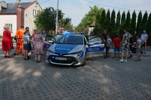 Na zdjęciu widoczny radiowóz z otawrtymi drzwiami oraz dzieci i osoby dorosłe zaglądające do środka pojazdu.