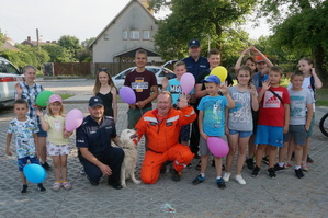 Zdjęcie grupowe, na którym widać dwóch umundurowanych policjantów, druha Ochotniczej Straży Pożarnej w Niegowonicach, dzieci oraz psa. Niektóre dzieci trzymają w rękach kolorowe balony.