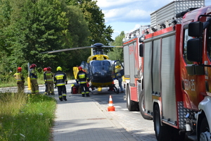 Na zdjęciu widoczne wozy strażackie. Nieco dalej widoczni strażacy oraz helikopter Lotniczego Pogotowia Ratunkowego.