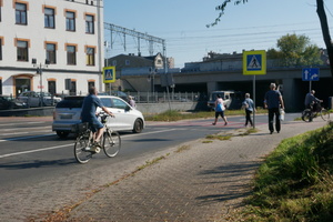 Na zdjęciu widać zartzymujący się przed przejściem dla pieszych samochód i jadącego rowerzystę. Przez pasy przechodzą osoby.