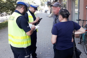 Na zdjęciu widoczni dwaj umundurowani policjanci rozmawiający z kobietą i mężczyzną.