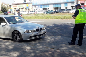 Na zdjęciu widoczny zatrzymany samochód osobowy i dwaj umundurowani policjanci przeprowadzający kontrolę drogową.