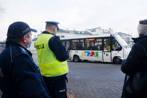 Na zdjęciu widoczni umundurowaniu policjanci i przedstawicielka Sanepidu. W tle autobus komunikacji miejskiej.