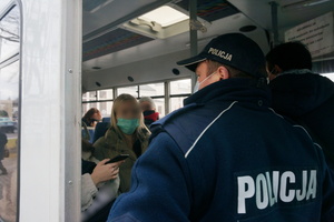 Na zdjeciu widoczny umundurowany policjant, który rozmawia wewnątrz busa z pasażerkami.