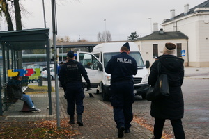 Dwaj umundurowani policjanci wraz z przedsatawicielką Sanepidu idą w kierunku busa.