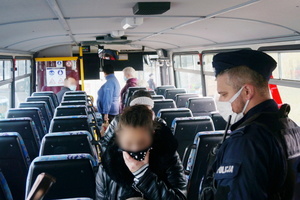 Na zdjęciu widoczny umundurowany policjant wewnątrz autobusu, który zwraca uwagę kobiecie na obowiązek zasłaniania ust i nosa. Kobieta ptrzytrzymuje ręką chustę, którą zakrywa usta i nos.