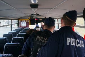 Na zdjęciu widoczni dwaj umundurowani policjanci wewnątrze autobusu. Policjanci obserwują, czy pasażerowie stosują się do obostrzeń.