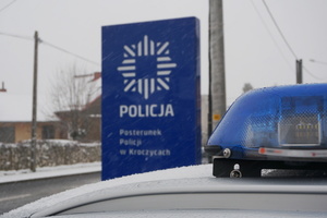 Częściowo widoczna sygnalizacja świetlna radiowozu na tle panelu infomacyjnego, na którym widoczna jest policyjna gwiazda i napis POLICJA Posterunek Policji w Kroczycach