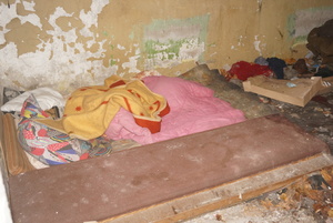 Na zdjęciu widoczne przygotowane w pustostanie miejsce do spania. Obok śmieci i pudełka.