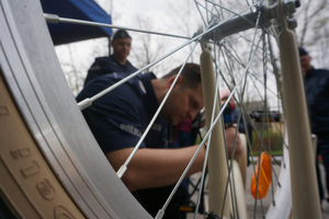 Przez rowerowe szprychy widać policjanta znakującego rower