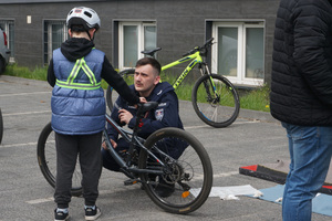 Policjant rozmawia z małym rowerzystą. Chłopiec ma kask ochronny i kamizelkę z elementami odblaskowymi