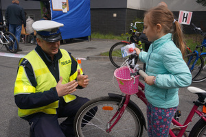 Policjant z zawierciańskiej drogówki rozmawia z dziewczynką trzymającą rower o bezpieczeństwie podczas jazdy jednośladem.