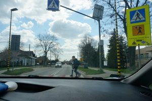 Widoczni chłopcy przechodzący przez przejście dla pieszych. Na zdjęciu widoczne także oznakowanie pionowe przejścia i samochód, który zbliża się do przejścia dla pieszych.