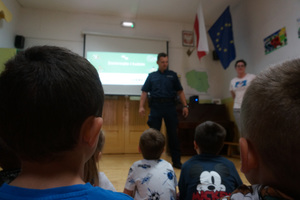 Dzieci słuchają policjanta, prowadzącego pogadankę