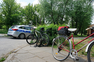 Dwa rowery stoją na chodniku. W tle widoczny radiowóz