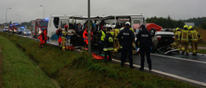 Na zdjęciu widać wypadek drogowy z autobusem, funkcjonariuszy Policji, Straż Pożarnej i poszkodowane osoby. W tle radiowozy na sygnałach błyskowych.