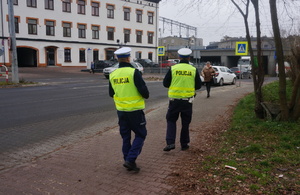 Zdjęcie przedstawia umundurowanych policjantów idących chodnikiem