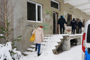 Zdjęcie kolorowe. Policjanci i strażnicy miejscy oraz przedstawicielka Miejskiego Ośrodka Pomocy Społecznej w Zawierciu wchodzą do pustostanu.