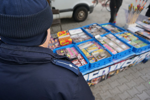 Zdjęcie kolorowe. Policjant kontroluje stoisko z fajerwerkami.