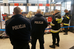 Zdjęcie kolorowe. Policjanci ze strażakami kontrolują stoisko z fajerwerkami.