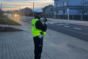 Na kolorowym zdjęciu widoczny umundurowany policjant dokonujący pomiaru prędkości.